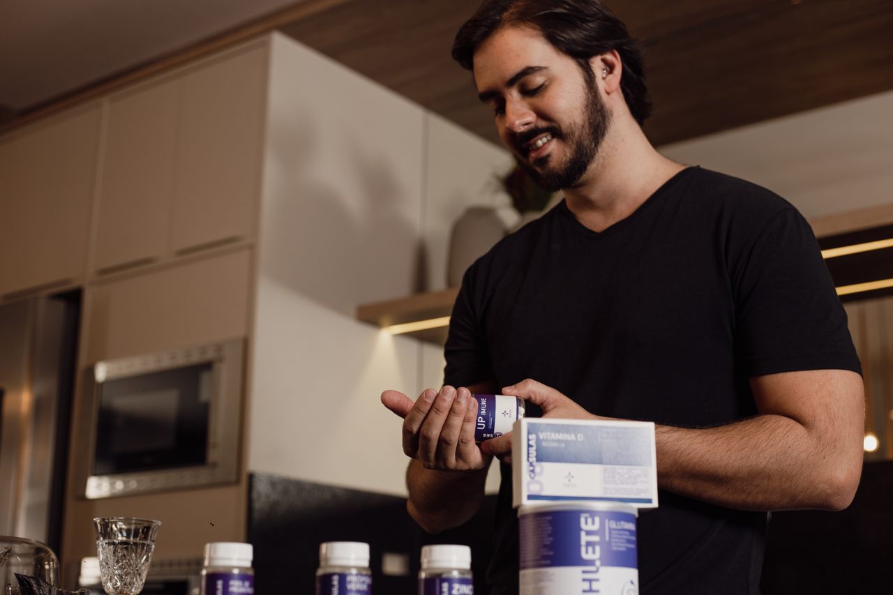 Man in kitchen holding and reviewing a bottle of supplements, indicating health-conscious lifestyle.